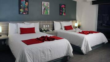 Habitación de hotel con dos camas, cada una con ropa blanca y almohadas rojas. Hay tres cuadros en la pared sobre las camas.