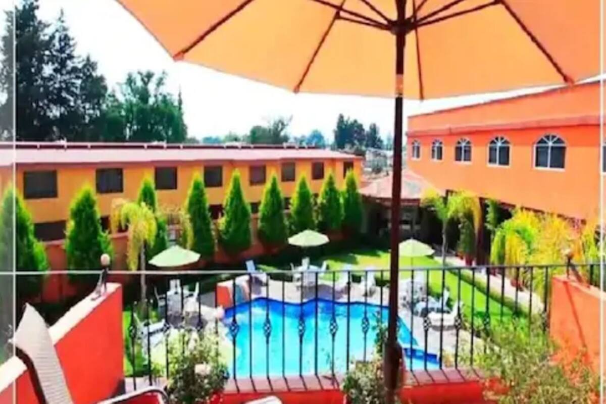 A pool area with a fenced pool, surrounded by greenery and a building with multiple windows.