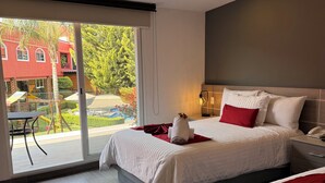 Habitación de hotel moderna con dos camas, un balcón y vistas a un edificio rojo y zonas verdes.