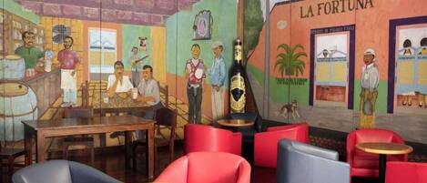 Interior de restaurante com um mural, assentos em vermelho e azul, e uma placa com 'La Fortuna'.