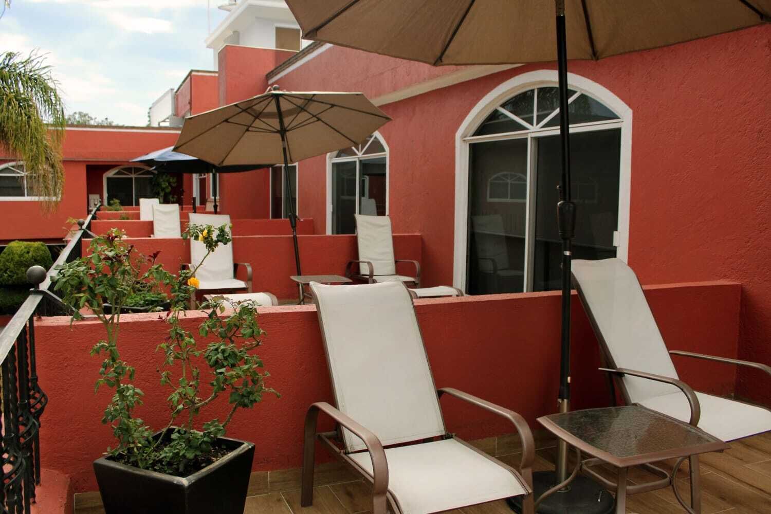 Une terrasse avec des chaises blanches et une table, une plante en pot et un grand parasol.