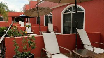 A patio with white chairs and a table, a potted plant, and a large umbrella.
