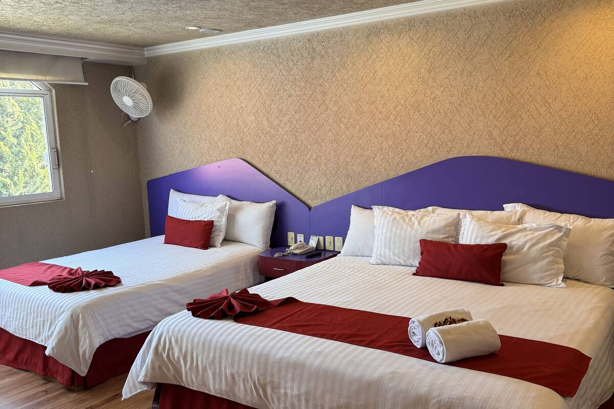 A hotel room with two beds, each with red and white bedding, a ceiling fan, and a window with a view of greenery.