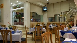 A restaurant with multiple tables and chairs, a television mounted on the wall, and a staircase in the background.