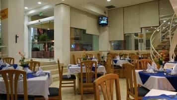 Un restaurante con varias mesas y sillas, un televisor en la pared y una escalera al fondo.