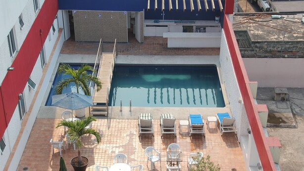 A rooftop pool area with a rectangular pool, lounge chairs, and a small table with chairs.