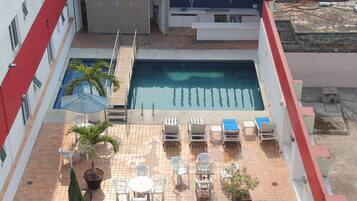 Un área de piscina en la azotea con una piscina rectangular, sillones de descanso y una pequeña mesa con sillas.