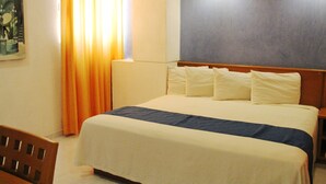 A hotel room with a bed, a headboard, a nightstand, a chair, a painting on the wall, and a window with curtains.