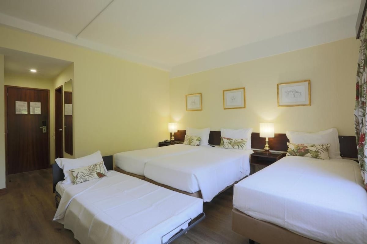 A hotel room with three beds, a wooden door, and framed pictures on the wall.