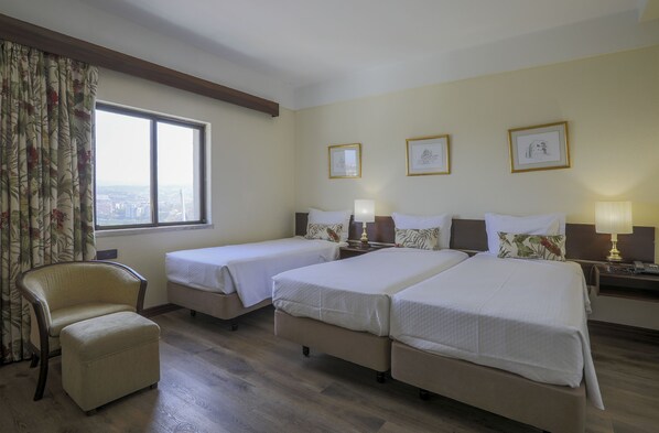 A hotel room with two single beds, a chair, and a large window with a city view.