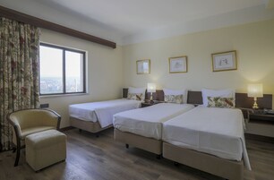 Habitación de hotel con dos camas individuales, una silla y un ventanal con vistas a la ciudad.