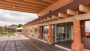 A covered outdoor area with a paved walkway, outdoor seating, and a view of a mountain in the background. - Parador (ZACATECAS)
