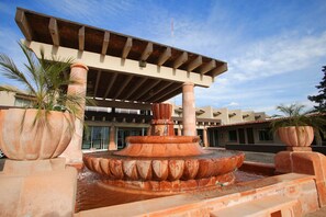 A fountain with a tiered design, surrounded by large planters and a building with a tiled roof in the background.