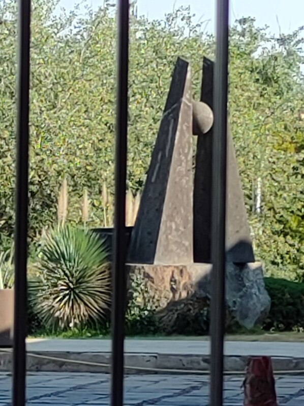A metal sculpture with abstract shapes and a backdrop of dense foliage.