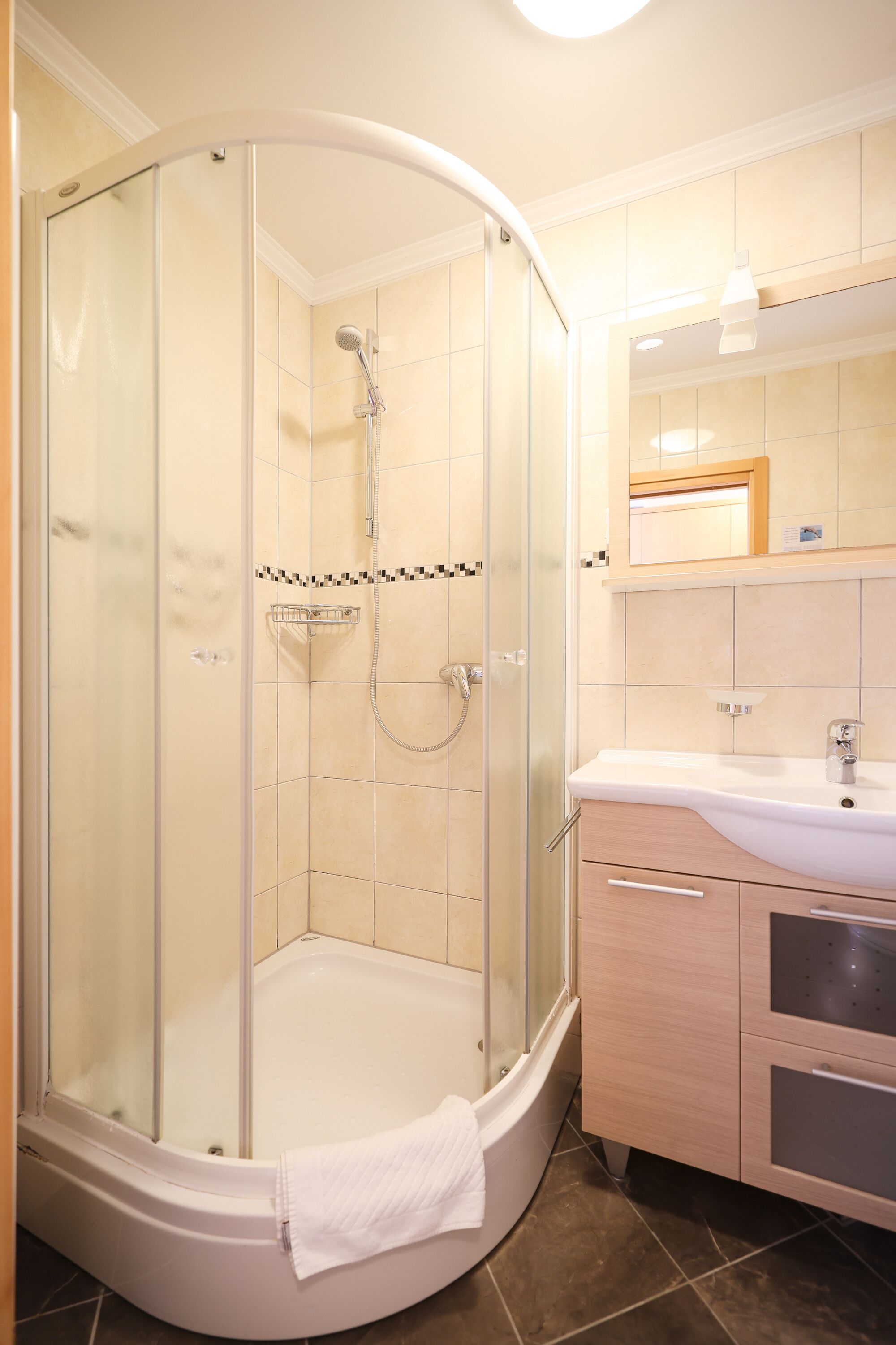 Un baño moderno con ducha cubierta por vidrio, un lavamanos blanco y un mueble de tocador de madera.