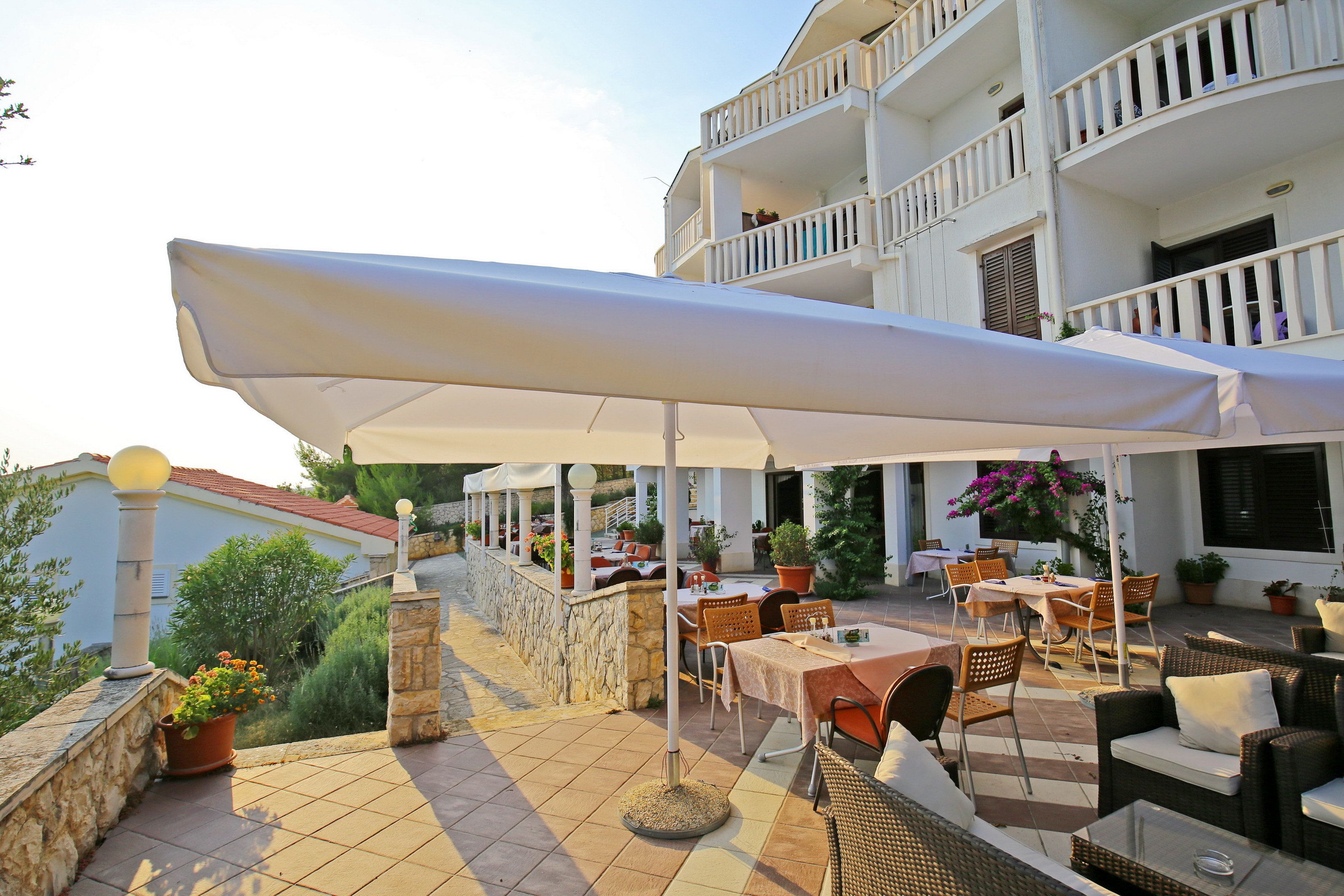 Een terras buiten met tafels en stoelen, een grote parasol en een stenen muur.