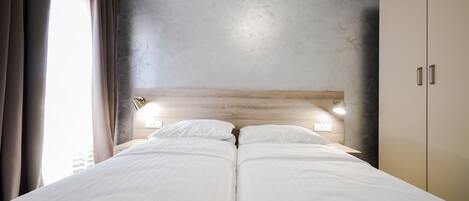 A double bed with white linens, a wooden headboard, and bedside lamps.