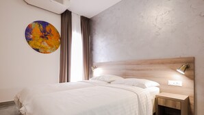 Ein modernes Schlafzimmer mit einem großen Bett, einem Nachttisch, einer Wandleuchte und einem farbenfrohen, abstrakten Gemälde.