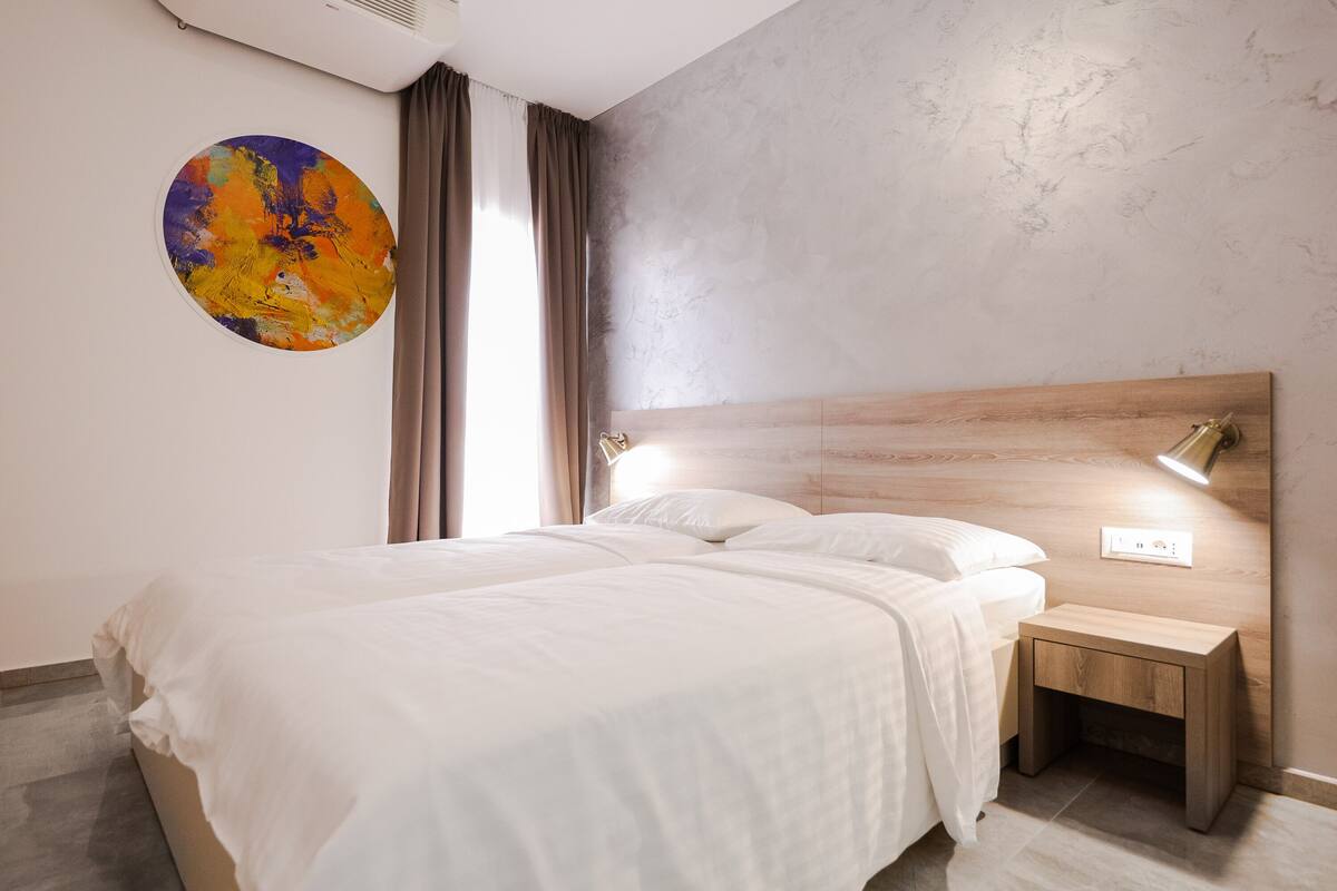 Un dormitorio moderno con una cama grande, una mesita de noche, una lámpara de pared y un cuadro abstracto colorido.