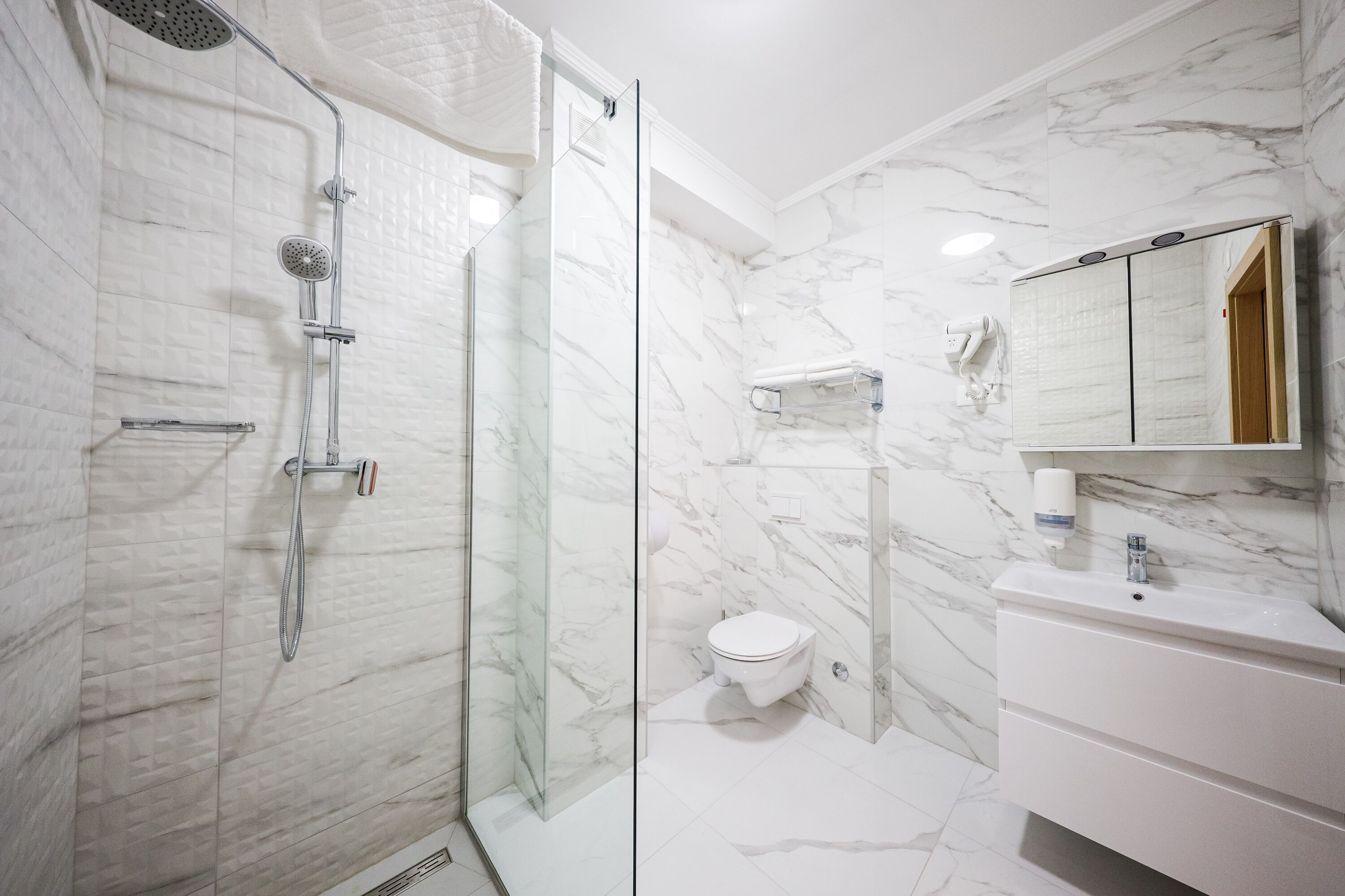 A modern bathroom with a glass-enclosed shower, a white toilet, and a marble wall.