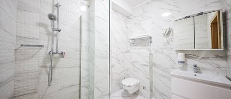 Een moderne badkamer met een douchecabine van glas, een wit toilet en een marmeren wand.