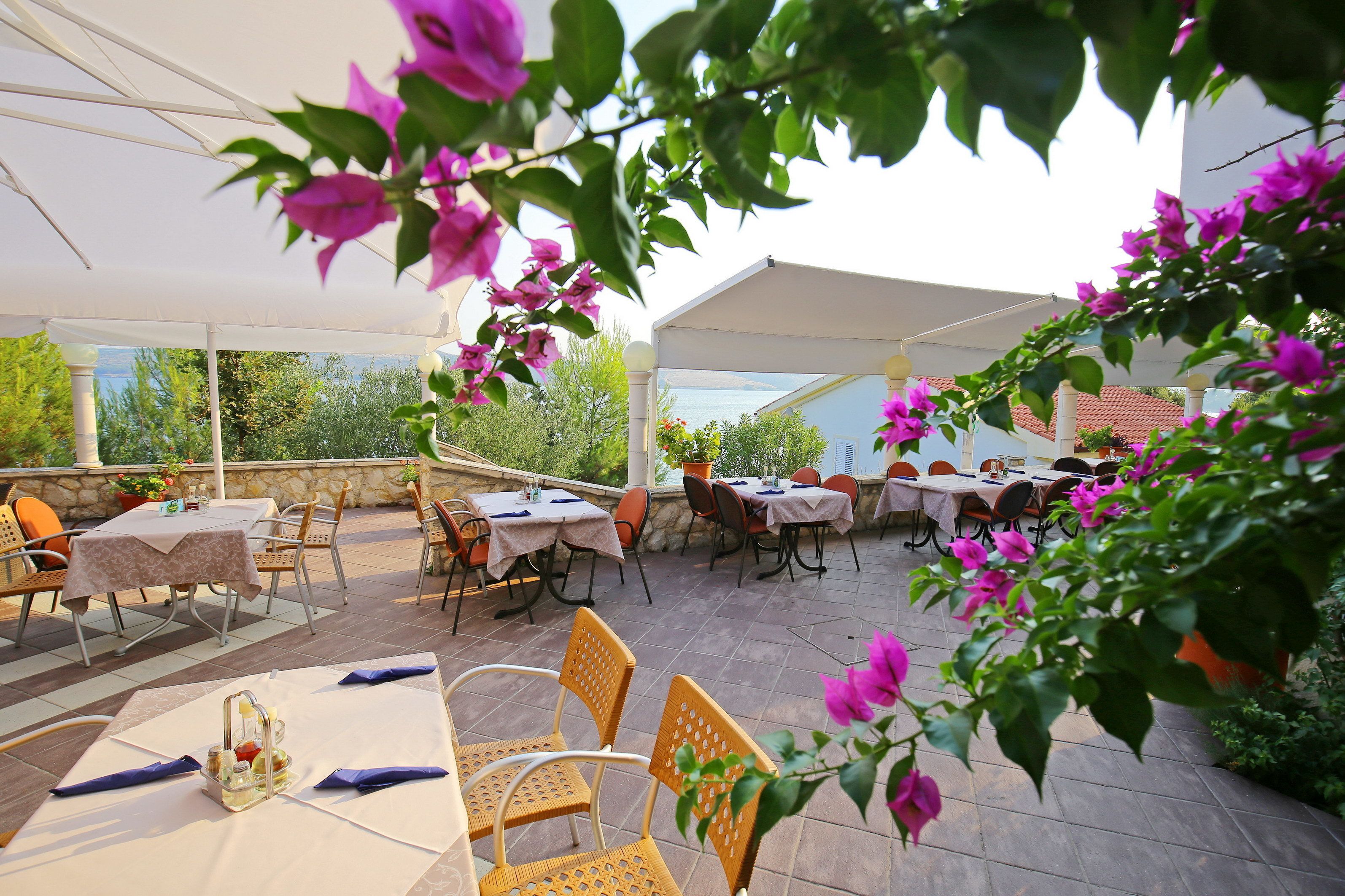 An outdoor patio area with tables and chairs, surrounded by a white canopy and potted plants.