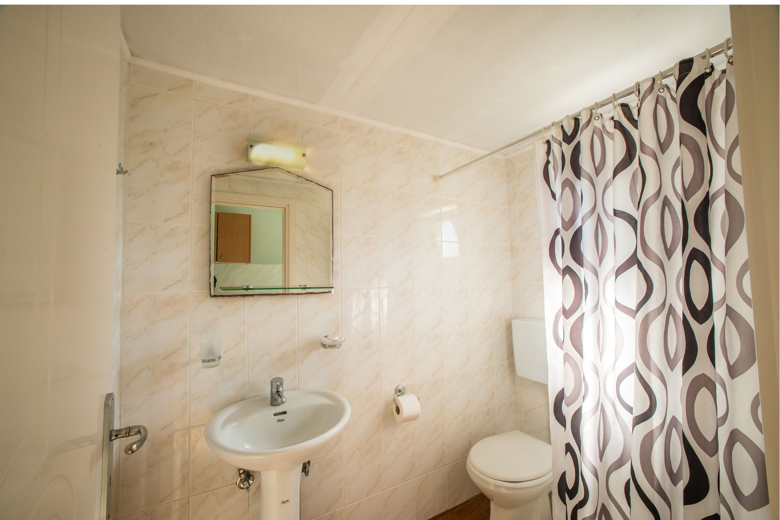 A bathroom with a sink, mirror, toilet, and patterned shower curtain.