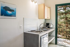 Una cucina compatta con lavastoviglie integrata, lavello e macchina per il caffè. Si vede una cornice con un'immagine appesa al muro e una vista su un balcone con ringhiera.
