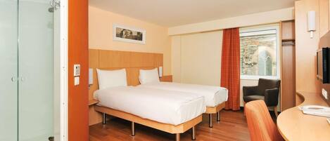 A hotel room with two beds, a desk, a chair, a television, and a window with a view of a building.