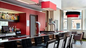 Un espace bar aux couleurs rouge et blanc, avec un comptoir, de nombreux sièges et une vue sur l’extérieur grâce à de grandes fenêtres.