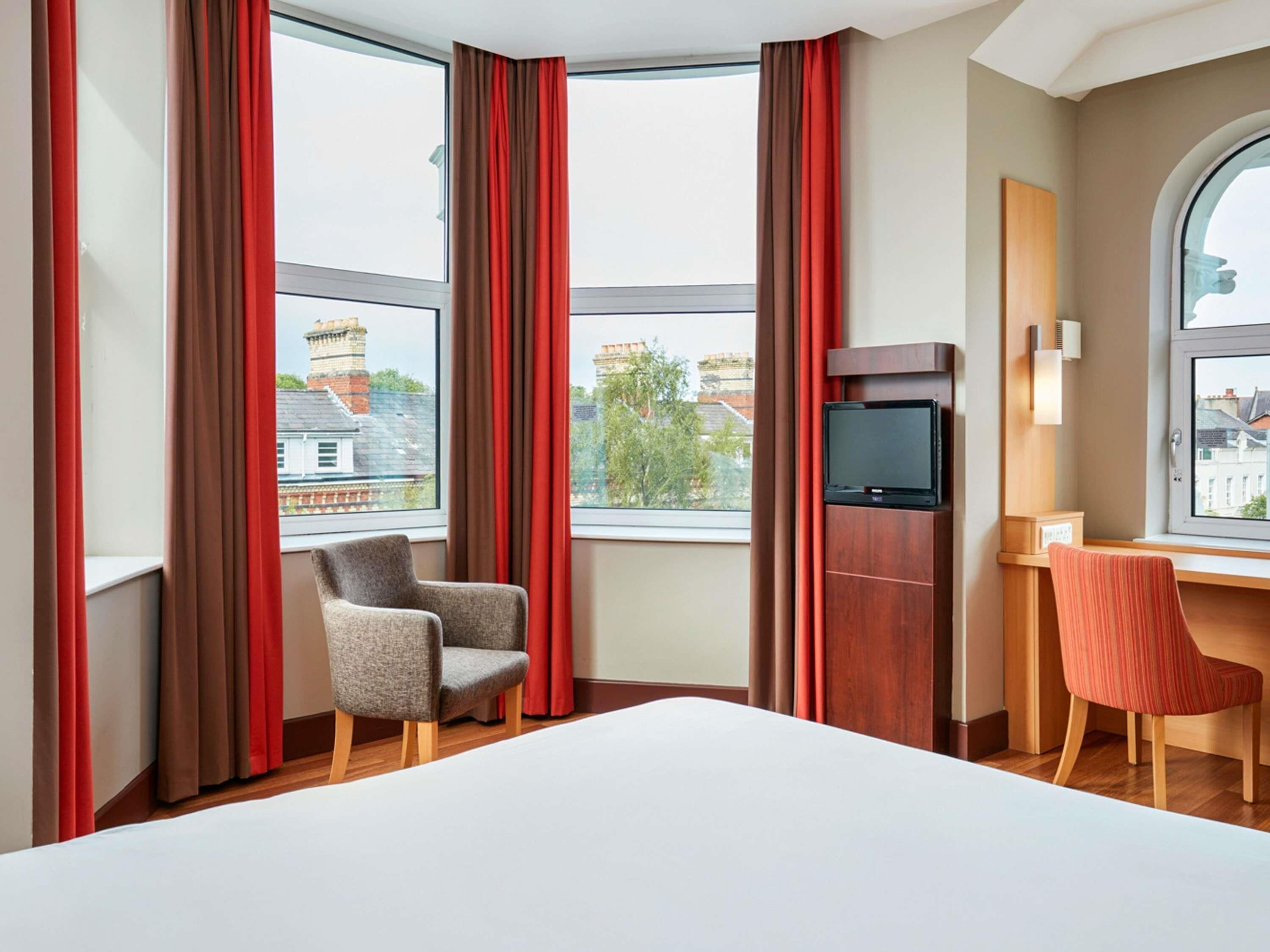 Ein Hotelzimmer mit einem Bett, einem Schreibtisch, einem Fernseher und zwei Stühlen.