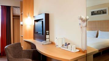 Habitación de hotel con escritorio, silla, cama, televisor, secador de pelo y teléfono.