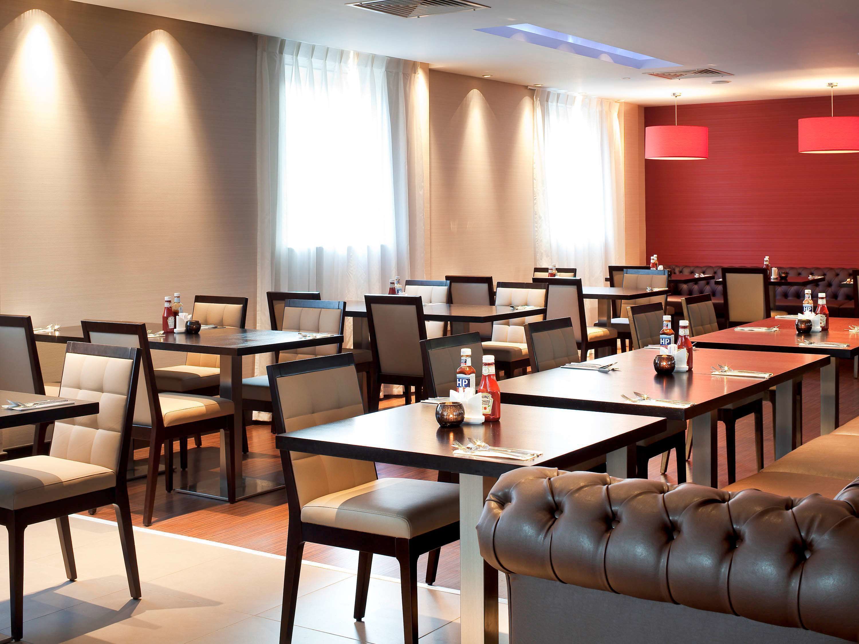 A hotel dining area with multiple tables and chairs, arranged in a spacious layout.