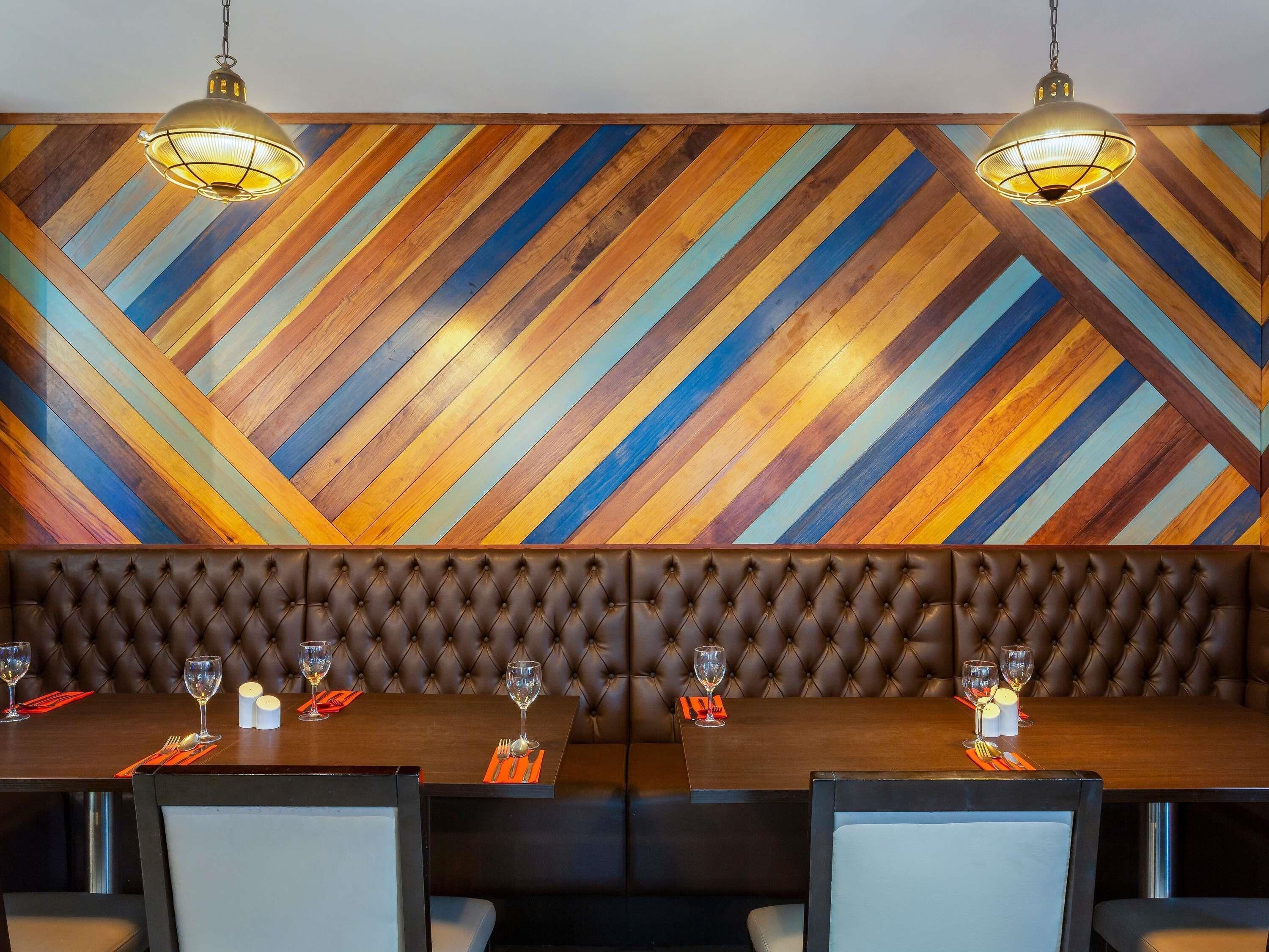 A dining area with a herringbone patterned wall, a tufted leather bench, and a table set with glasses and cutlery.