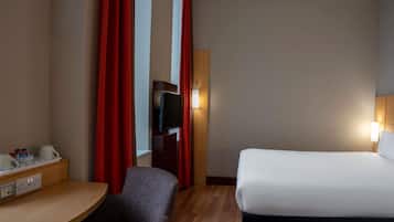 Ein Hotelzimmer mit einem Bett, einem Schreibtisch mit Stuhl, einem Fernseher und einer Lampe.