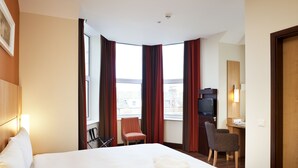 Une chambre d’hôtel avec un grand lit, un bureau avec une chaise, une télévision et une fenêtre avec des rideaux.