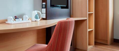 A hotel room with a wooden desk, a television, a red chair, and a wardrobe.