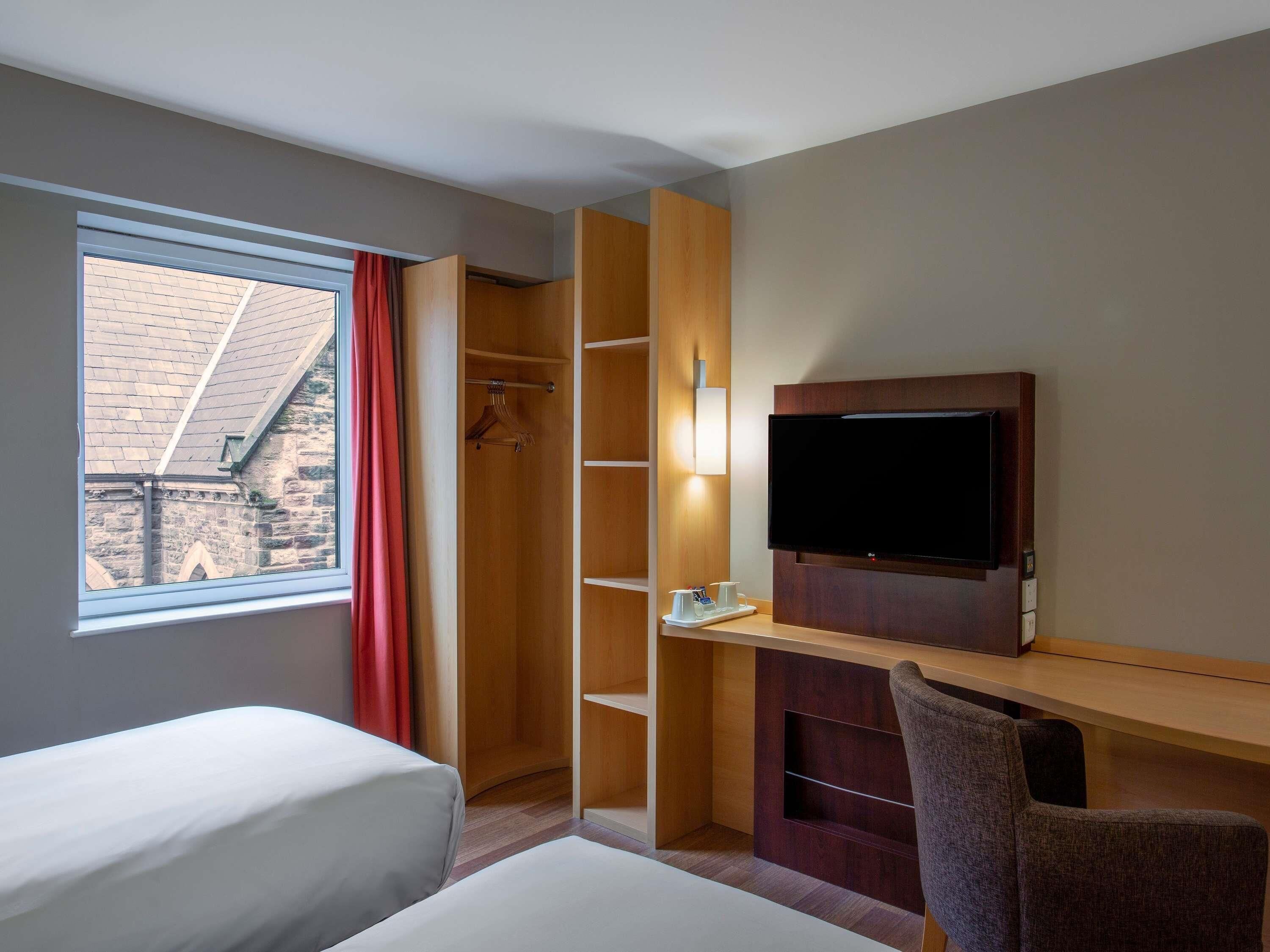Una habitación de hotel con una cama, un escritorio con televisor, una silla y un armario.