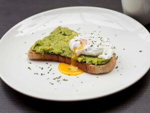 A plate with a slice of toast topped with avocado and a poached egg, garnished with herbs. - ibis Belfast Queens Quarter (Belfast)
