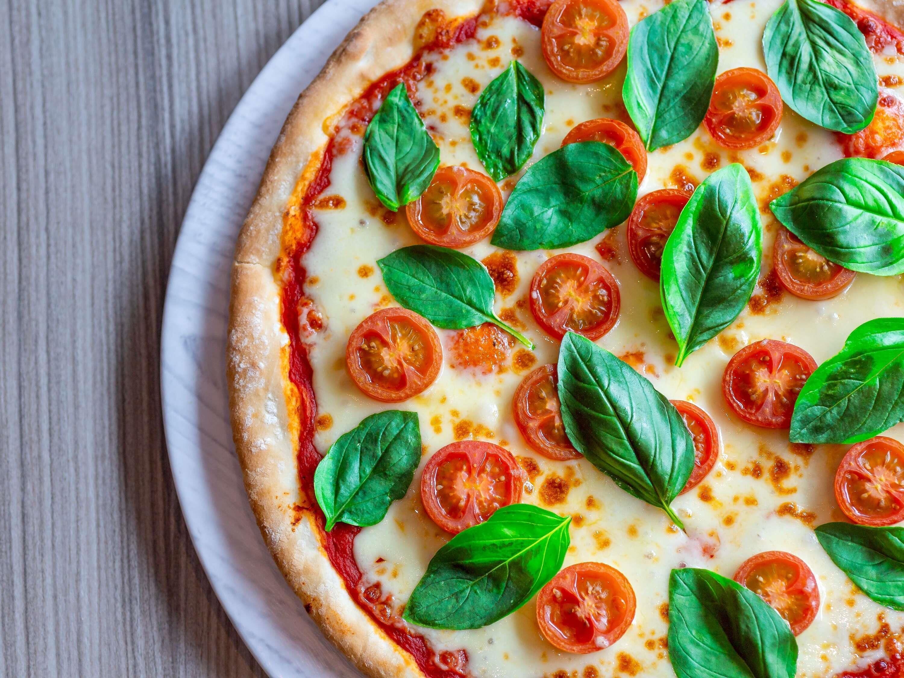 Pizza con rodajas de tomate y hojas de albahaca sobre un plato blanco.