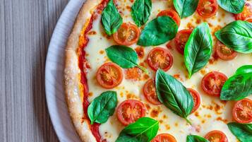 Pizza con rodajas de tomate y hojas de albahaca sobre un plato blanco.