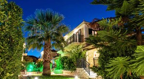 A multi-story building with a balcony, surrounded by lush greenery and palm trees.