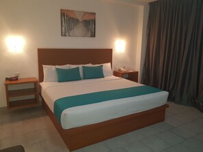 Una habitación de hotel con una cama grande, una mesita de noche, un cuadro en la pared y una cortina.