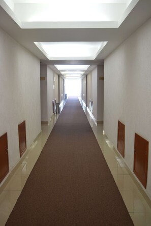 Un largo pasillo vacío de hotel con alfombra marrón, paredes blancas y puertas de madera.