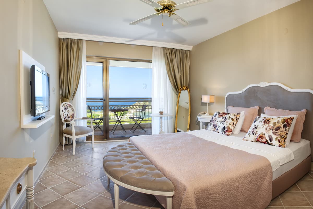 A hotel room with a bed, a TV, a balcony with a view, and a ceiling fan.