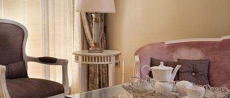 A living room with a glass coffee table, a brown armchair, a white side table with a lamp, and a pink sofa.