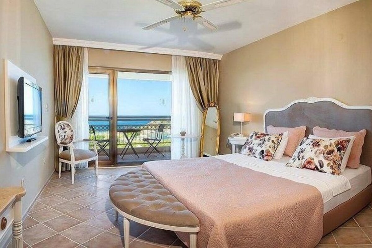 A hotel room with a bed, a television, a chair, a table, and a balcony with a view.
