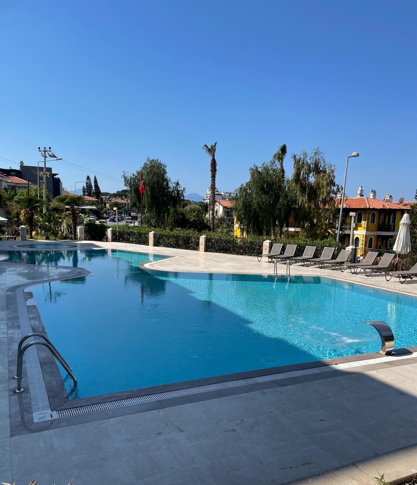 A swimming pool with a clear blue water, surrounded by lounge chairs and a flag.