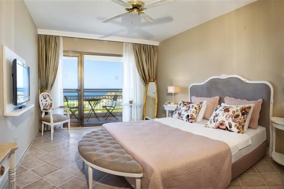 A hotel room with a large bed, a television, a balcony with a view, and a ceiling fan.