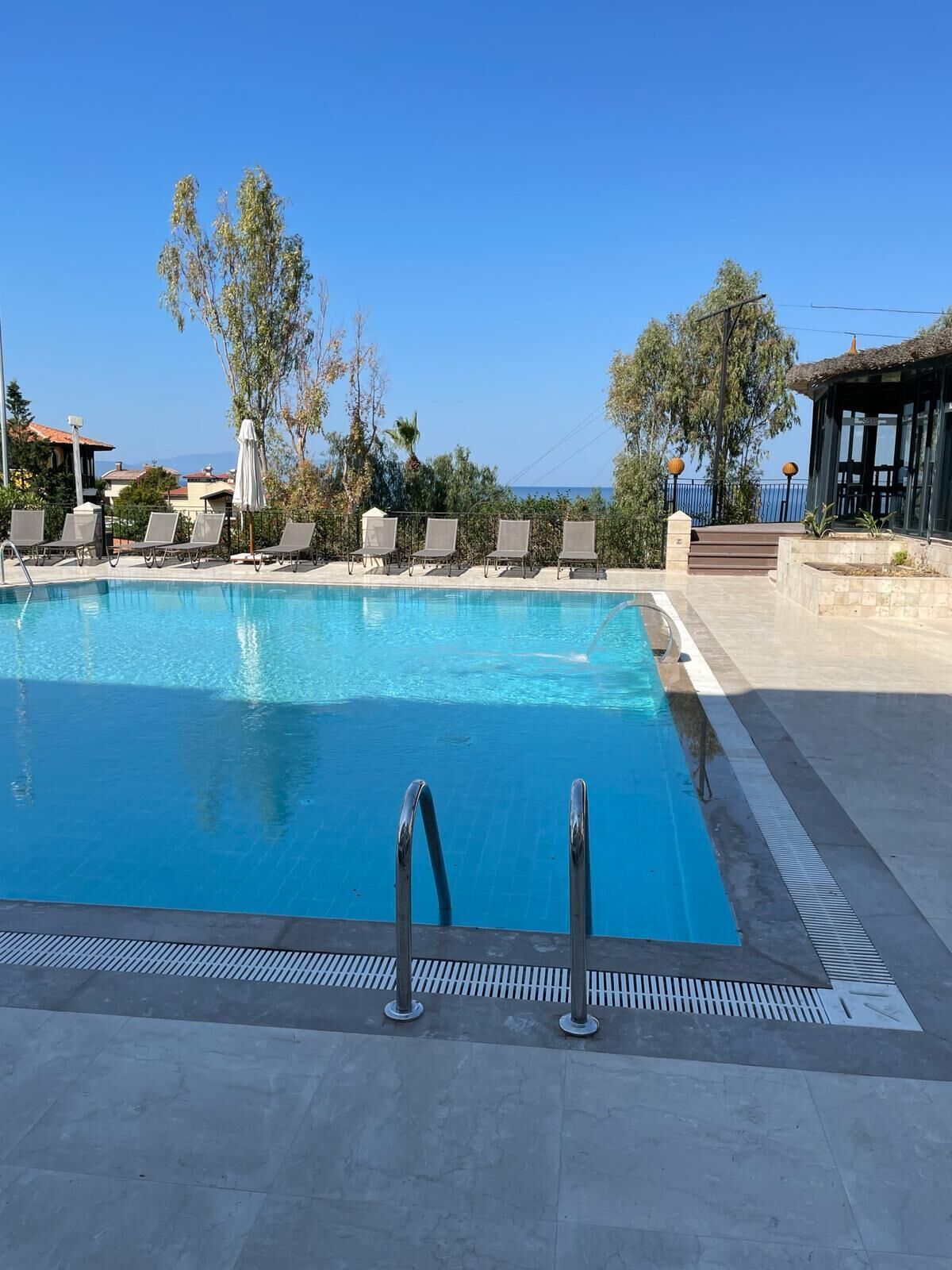Piscina azul límpida com espreguiçadeiras e área de estar coberta.